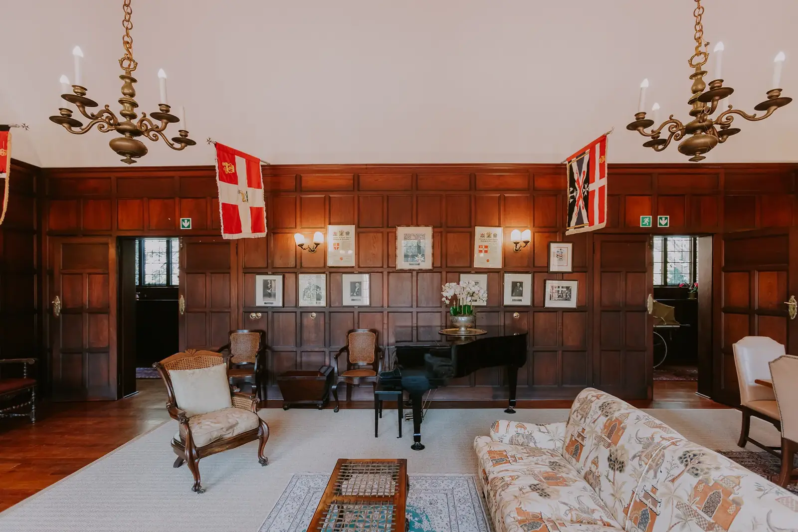The Council Room at Glenshiel, panelled, with a piano, portraits and chandeliers